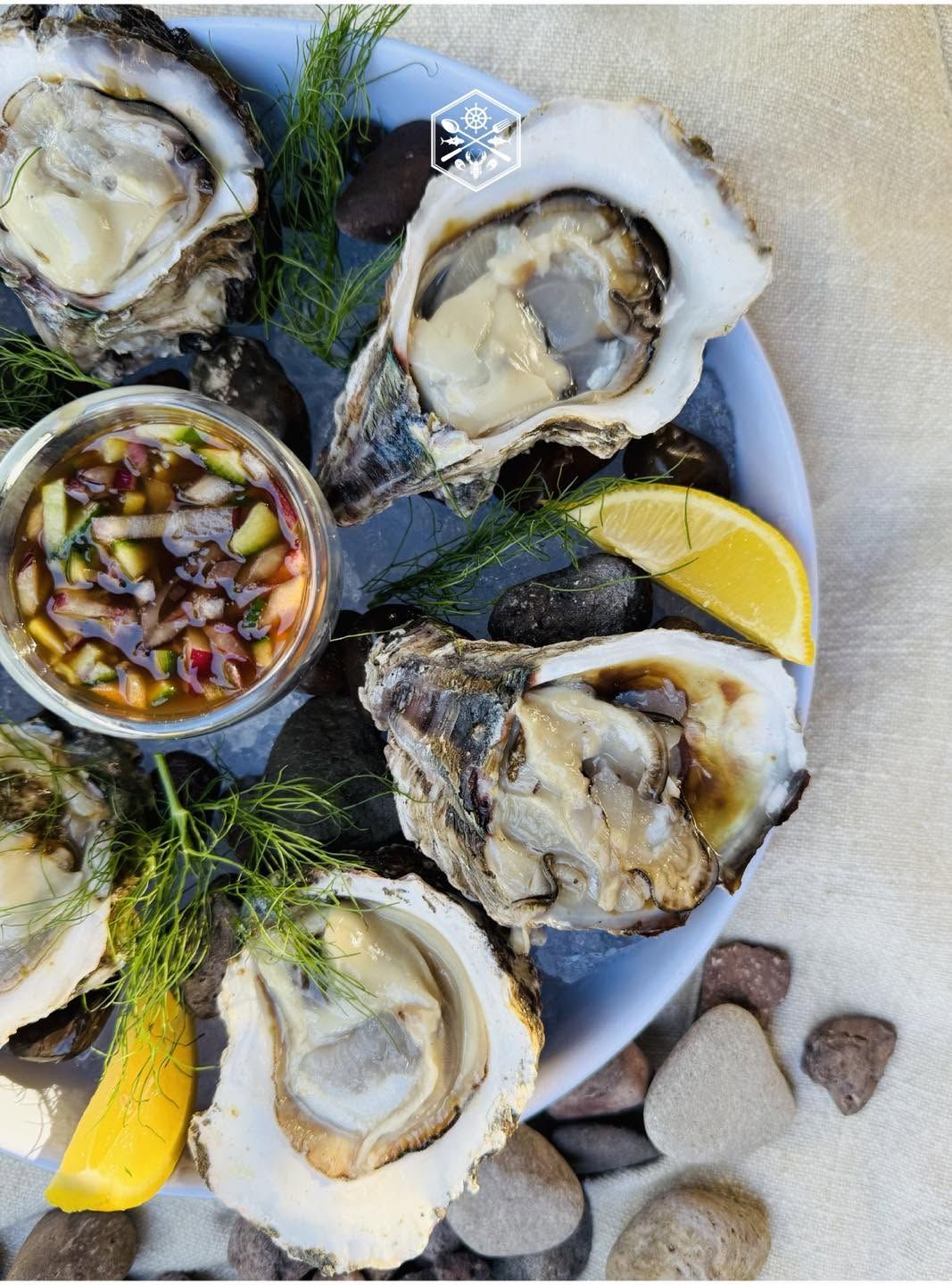 Fresh oysters on ice with lemon wedges and a small cup of mignonette sauce on a plate