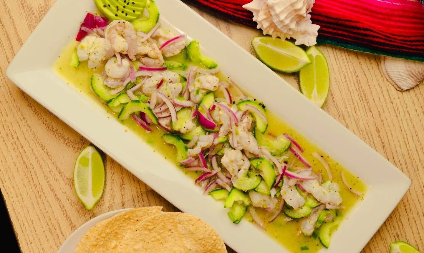 Ceviche on a rectangular white plate with lime wedges, red onions, and herbs on a wooden table