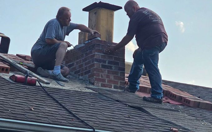 Two men are working on a chimney on top of a roof.