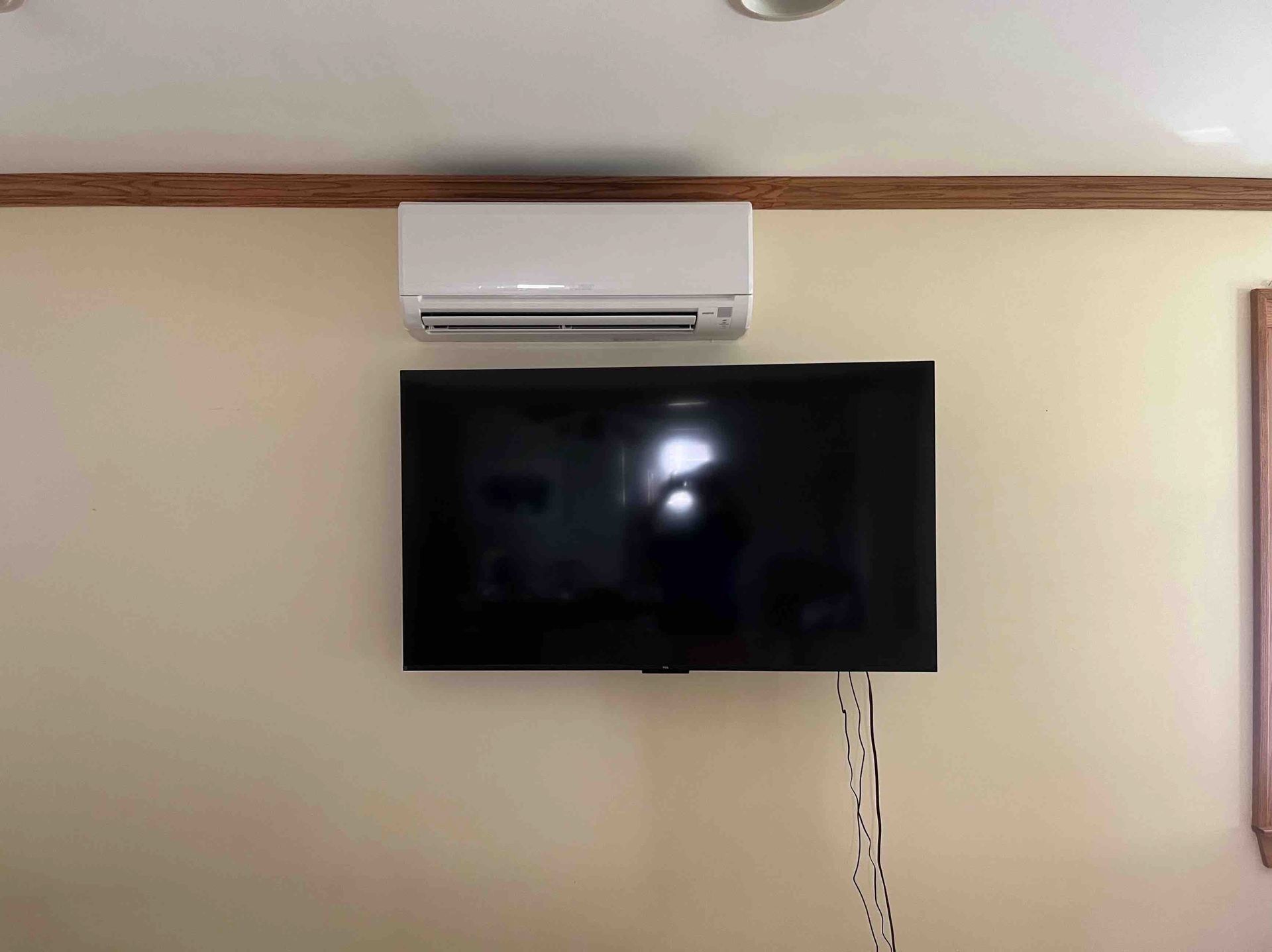 White air conditioner above a mounted black television on a tan wall.
