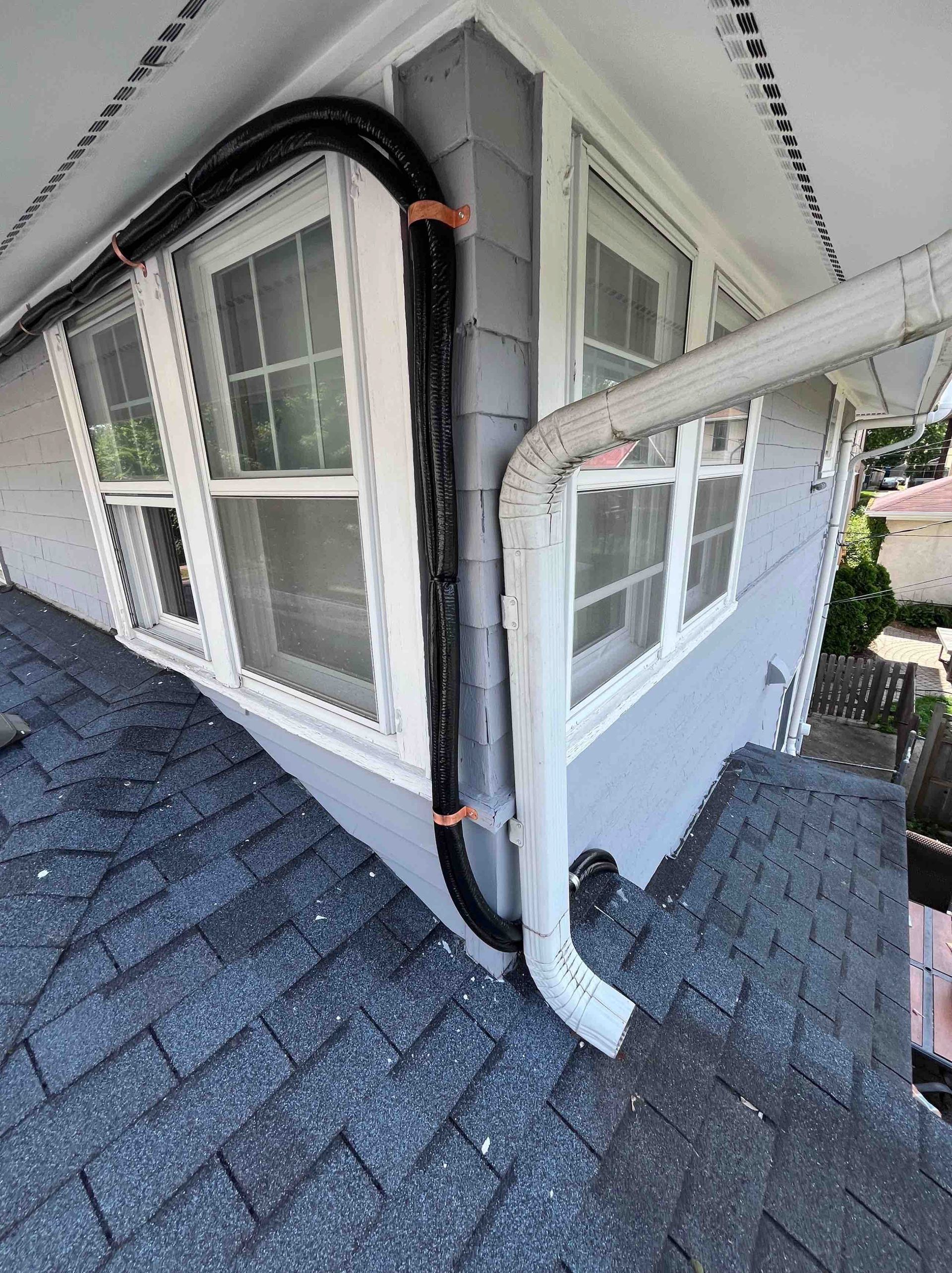 Black cable running along gray house exterior, secured with orange straps, near a gutter.