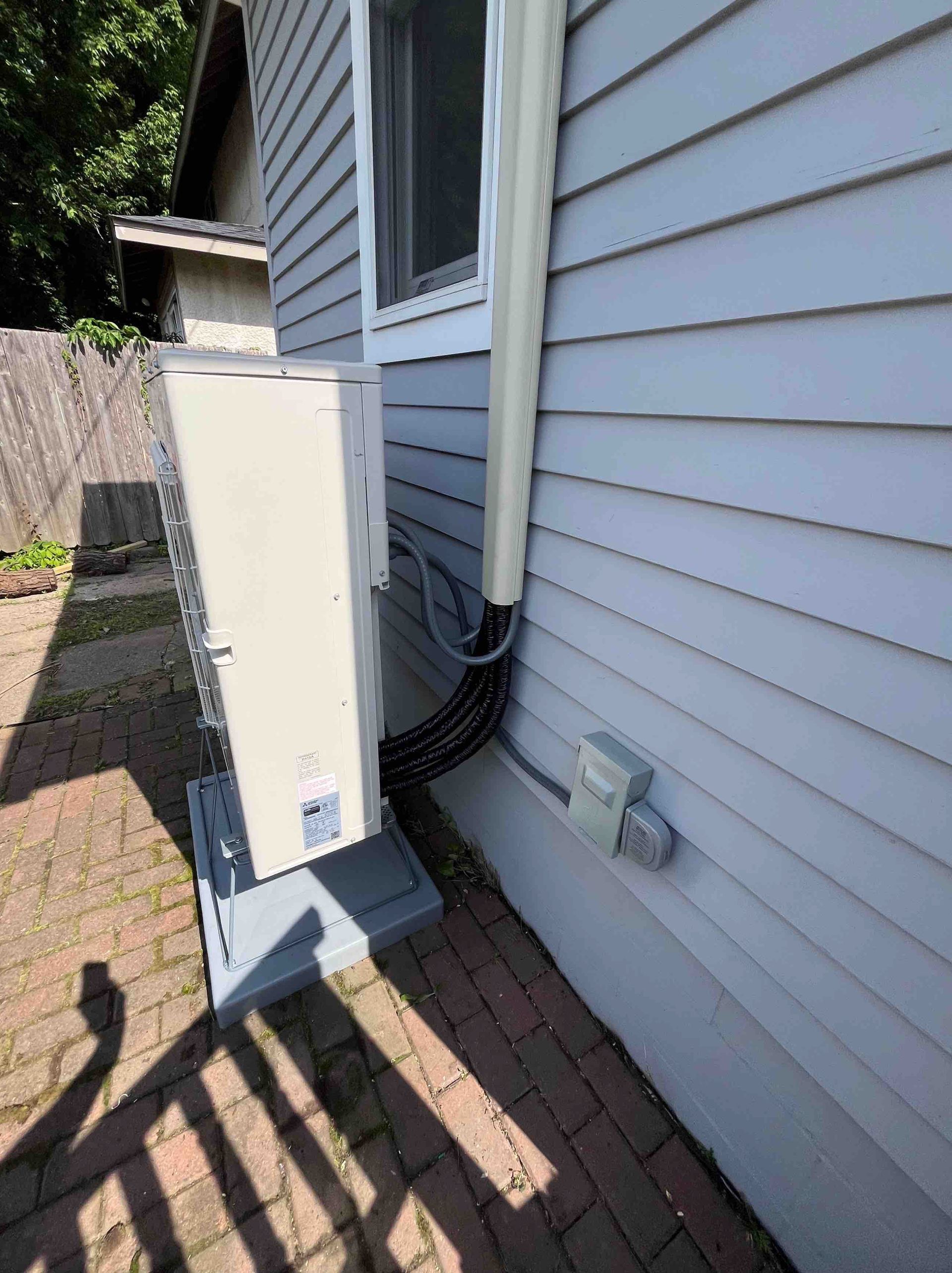 Exterior view: Air conditioning unit next to a light blue house with electrical components.