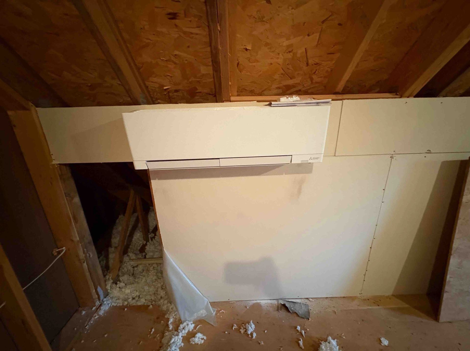 Interior view of a partially constructed wall in an attic, drywall is installed, exposed wood beams are visible.