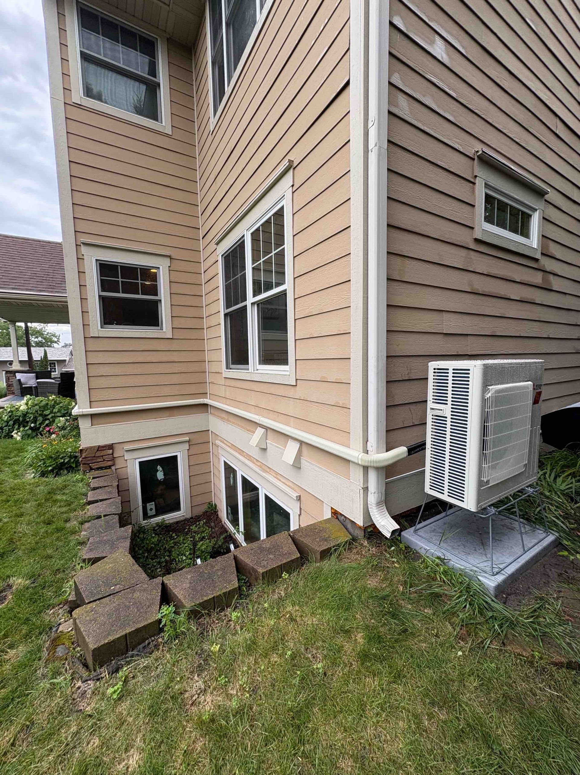 Tan house exterior with several windows and a ground-level basement window. An air conditioner is installed.