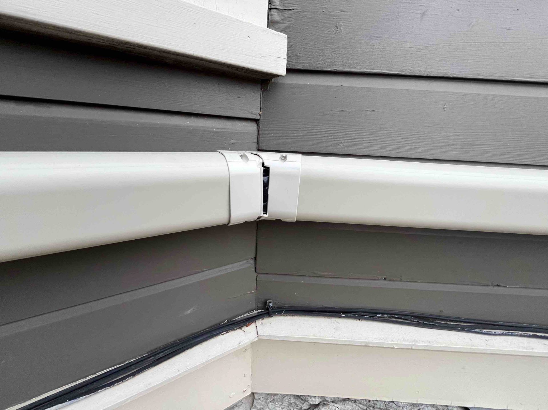 White gutter sectioned and joined at a corner on gray siding.