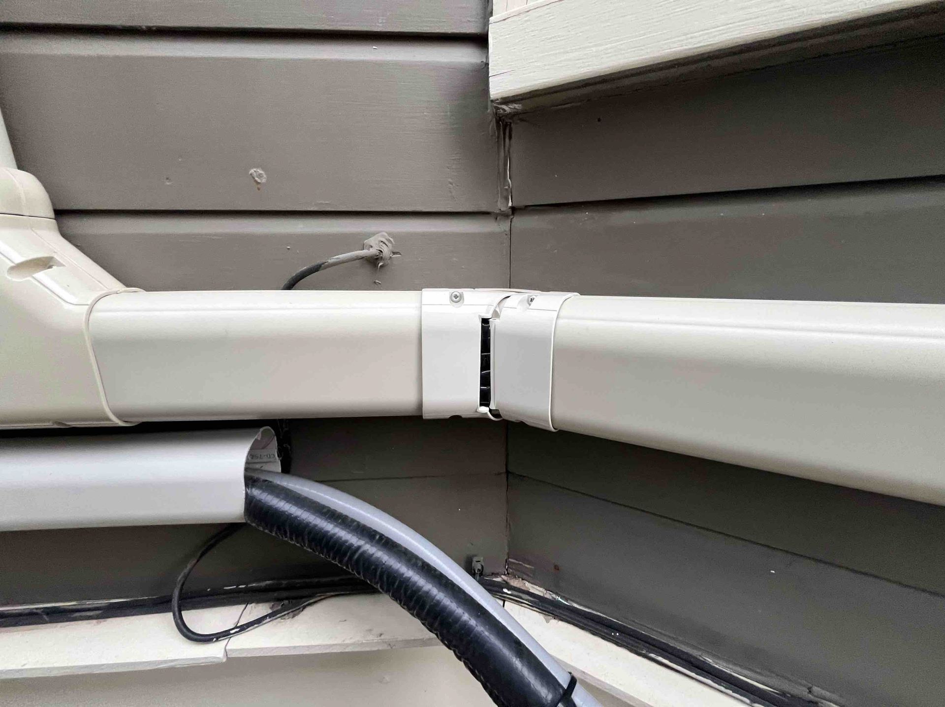 Gray gutter section connected at corner with a black hose emerging from a hole.