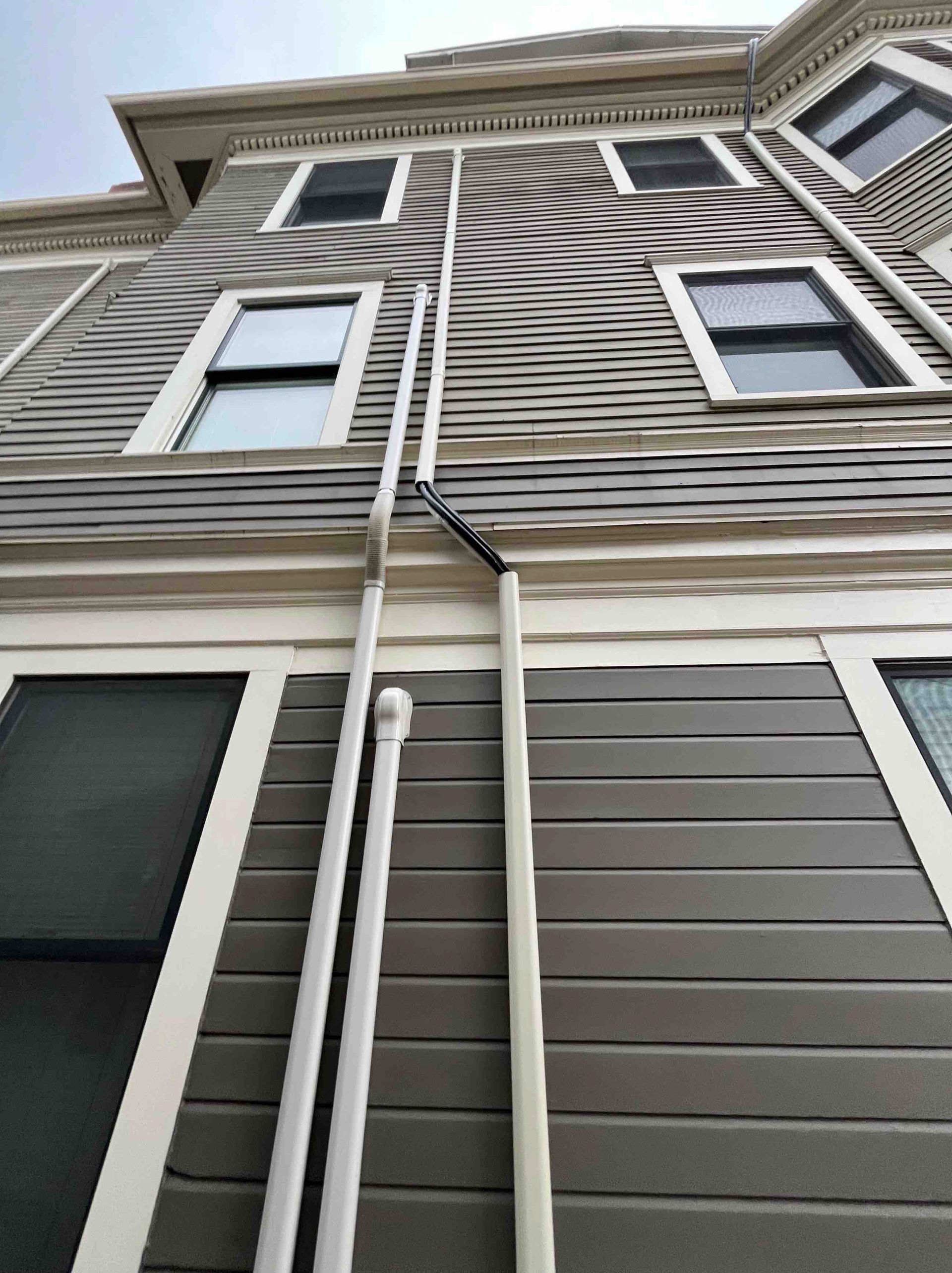 Exterior of a multi-story building with gray siding and white trim, visible from a low-angle perspective.