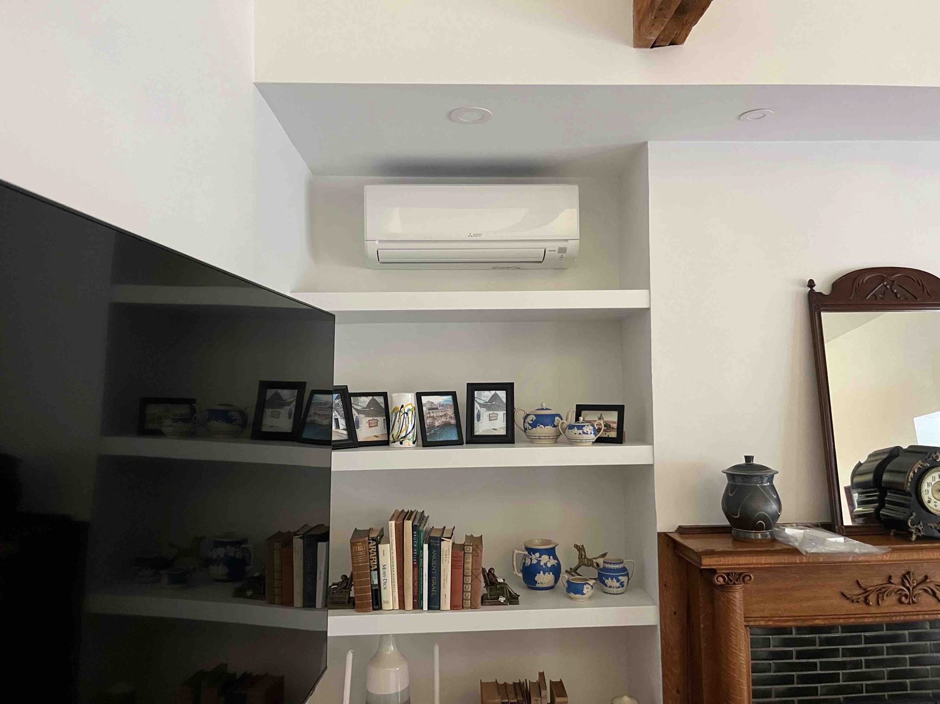 Air conditioner above built-in shelves with decor, in a white-walled room.