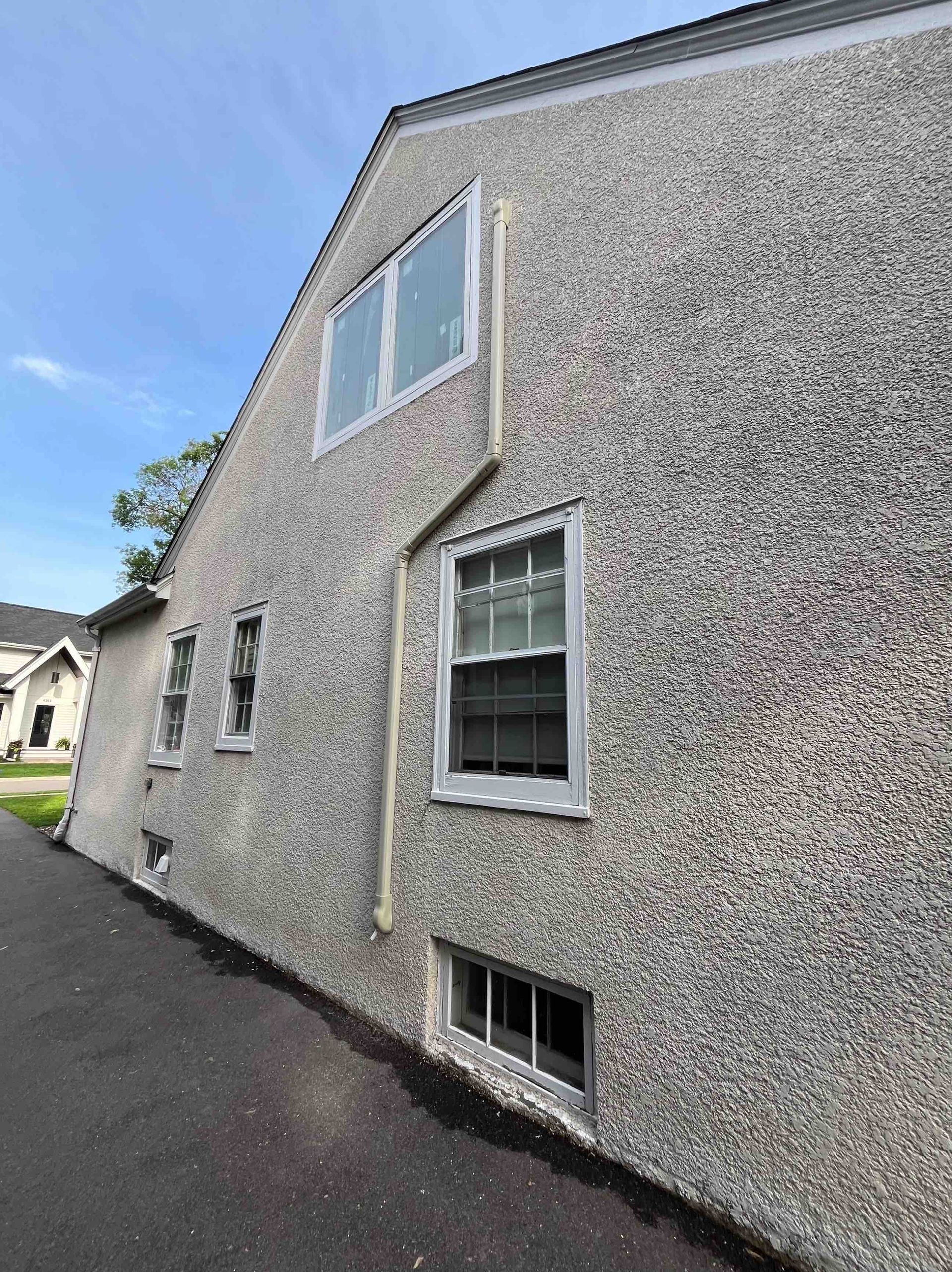 Gray textured house exterior with windows, light-colored trim, and dark asphalt driveway.