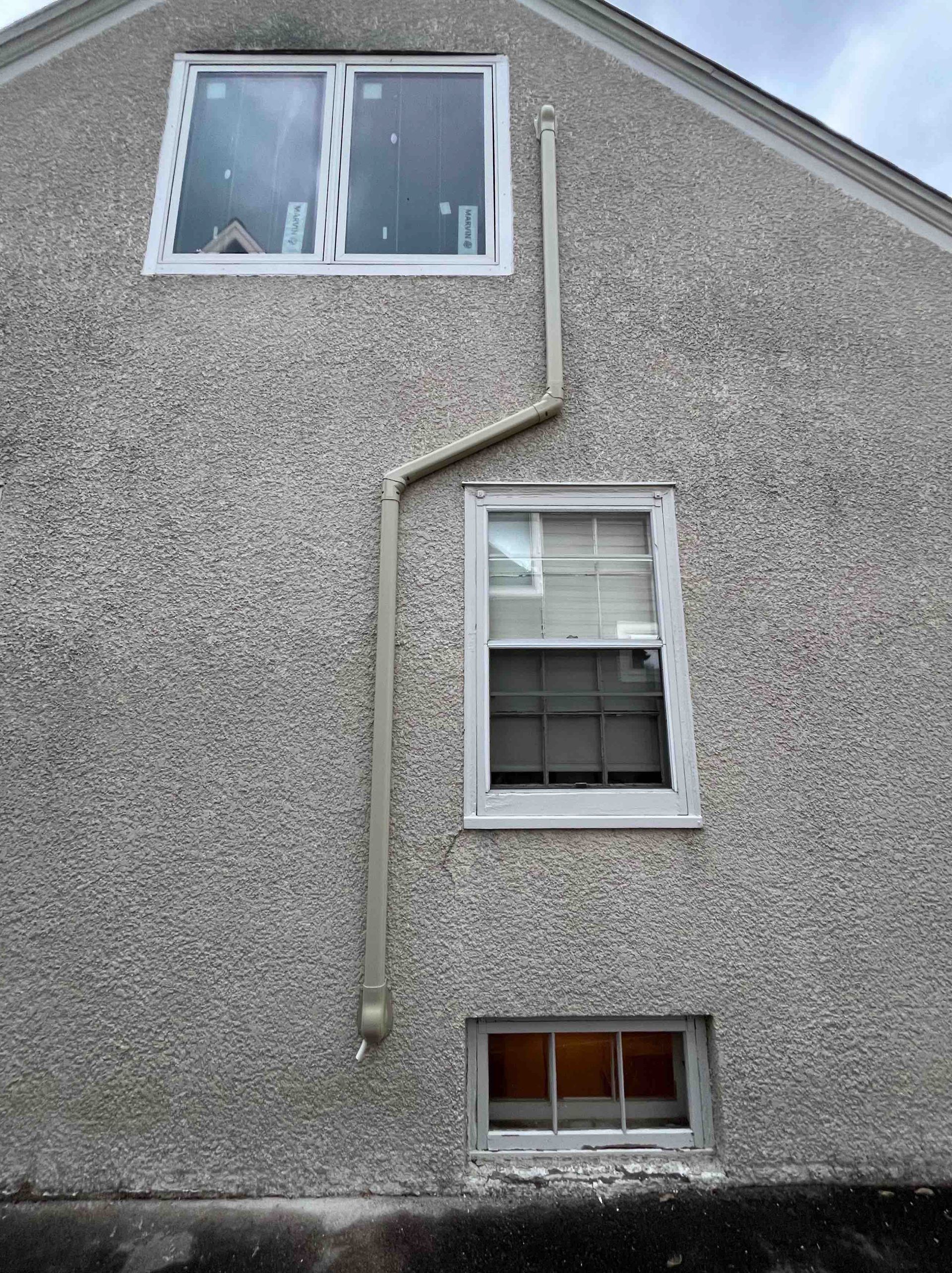 Gray stucco building exterior with windows and a downspout.