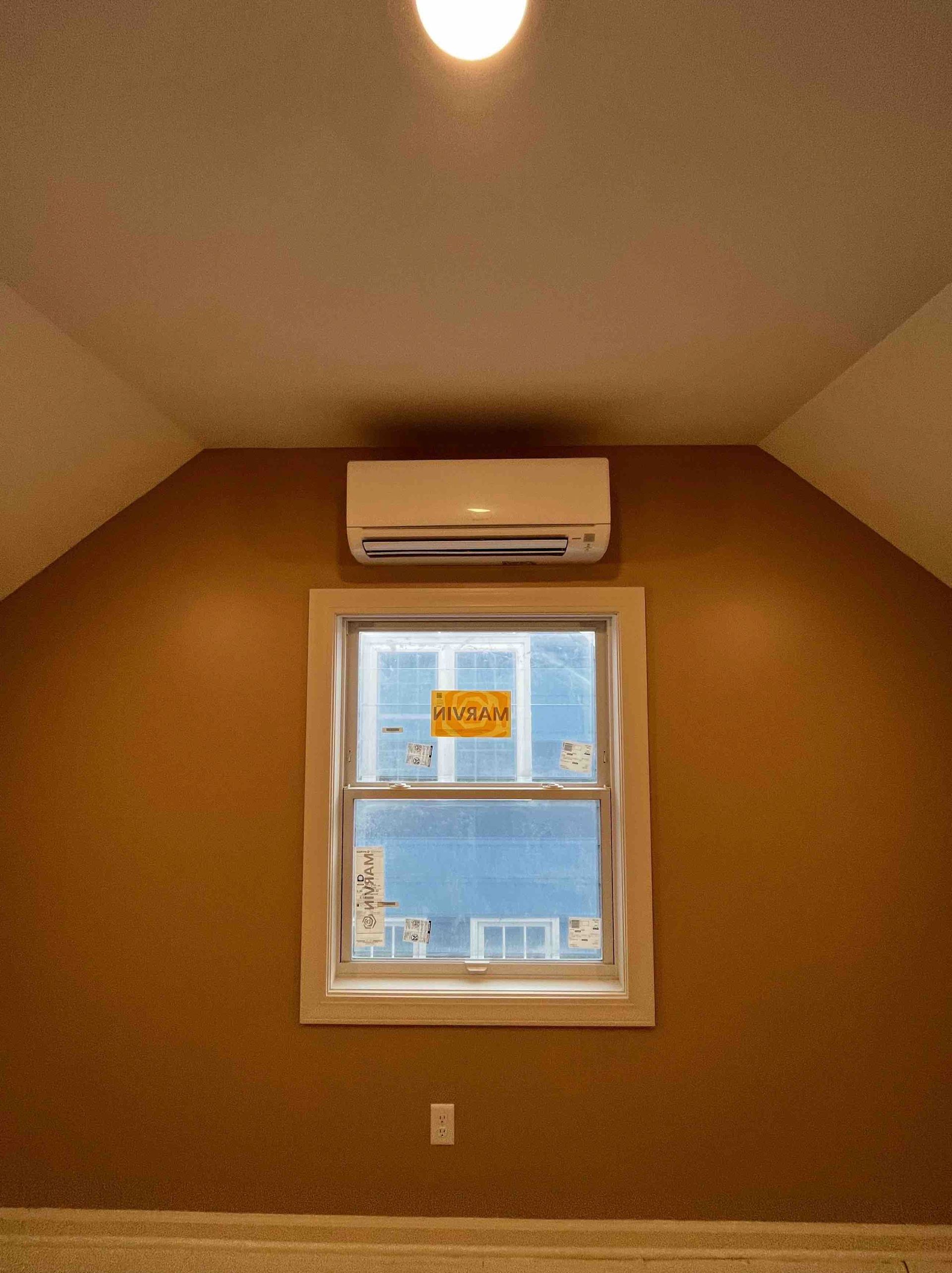 Interior room with brown walls and a white window; a white air conditioner sits above the window.