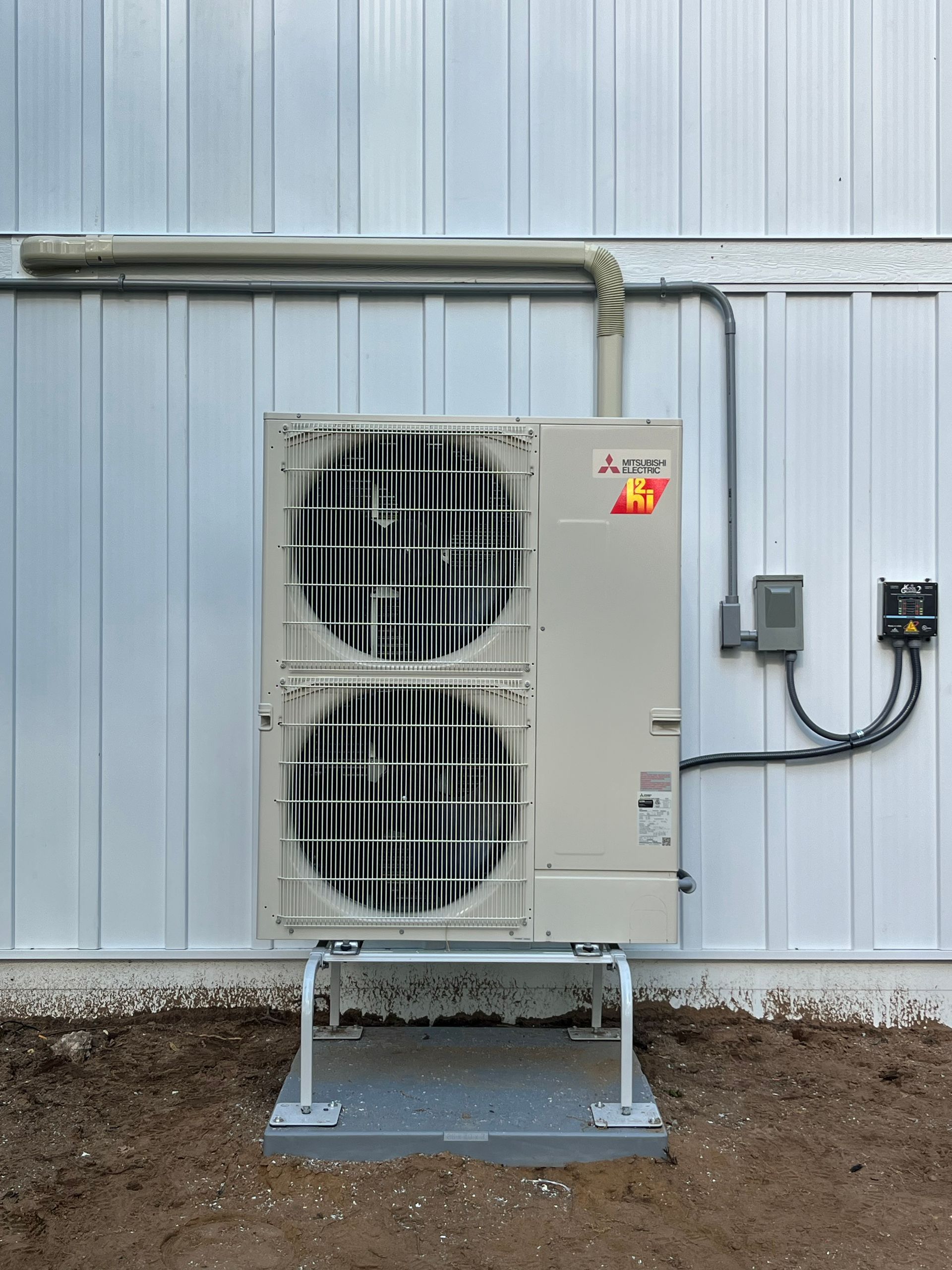 Mitsubishi heat pump unit mounted outside on a white metal building.