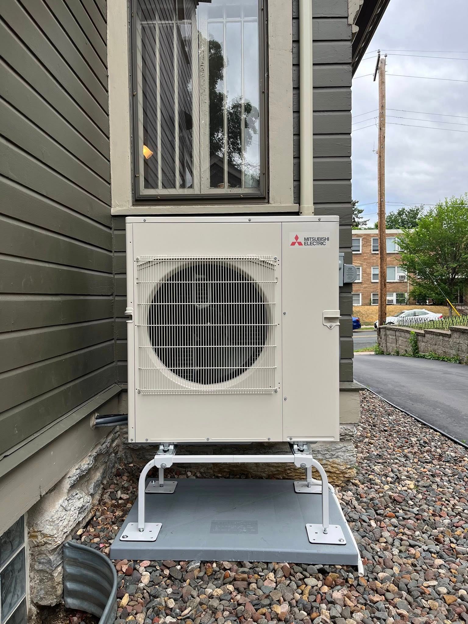 Mitsubishi heat pump mounted outside a building, on a gravel base.