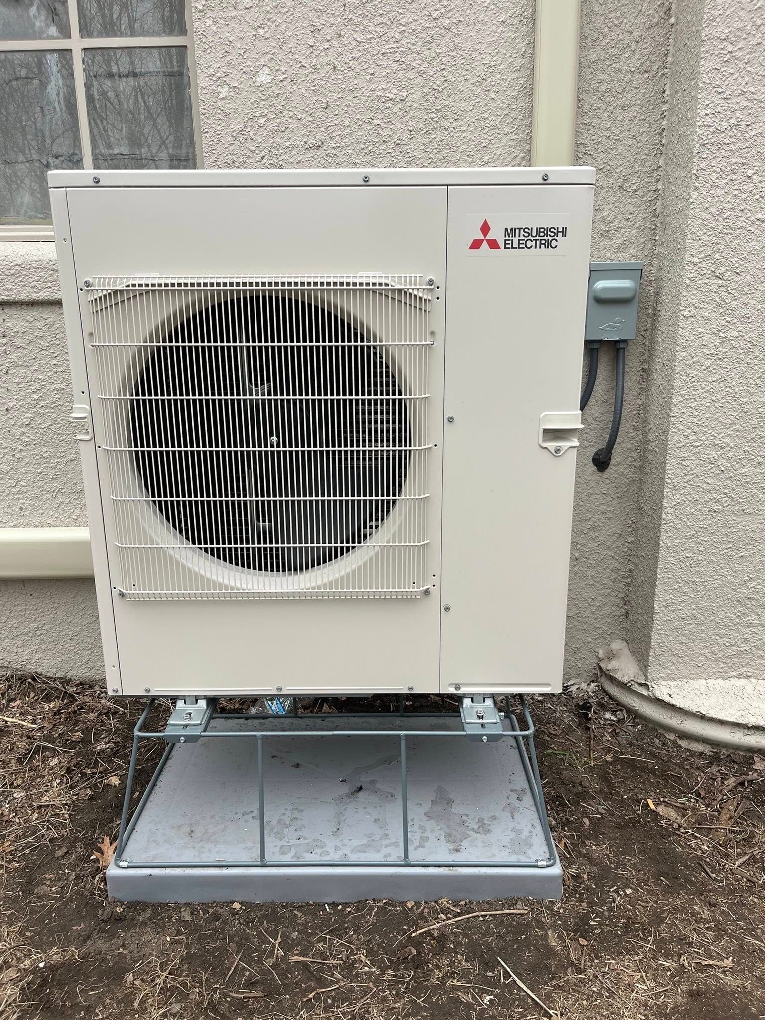 Mitsubishi heat pump unit mounted outdoors on a metal platform.