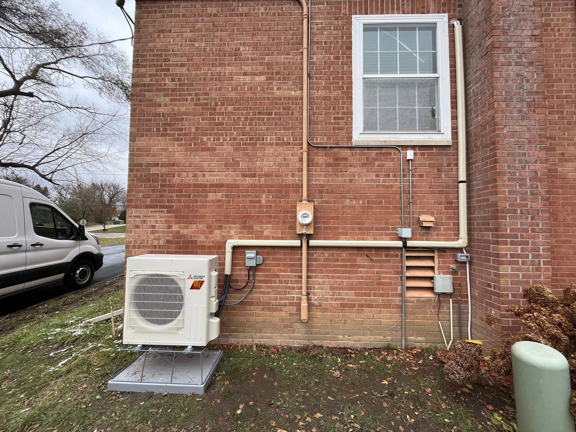 Exterior view of brick building with an air conditioning unit. Electrical conduit and window are visible.