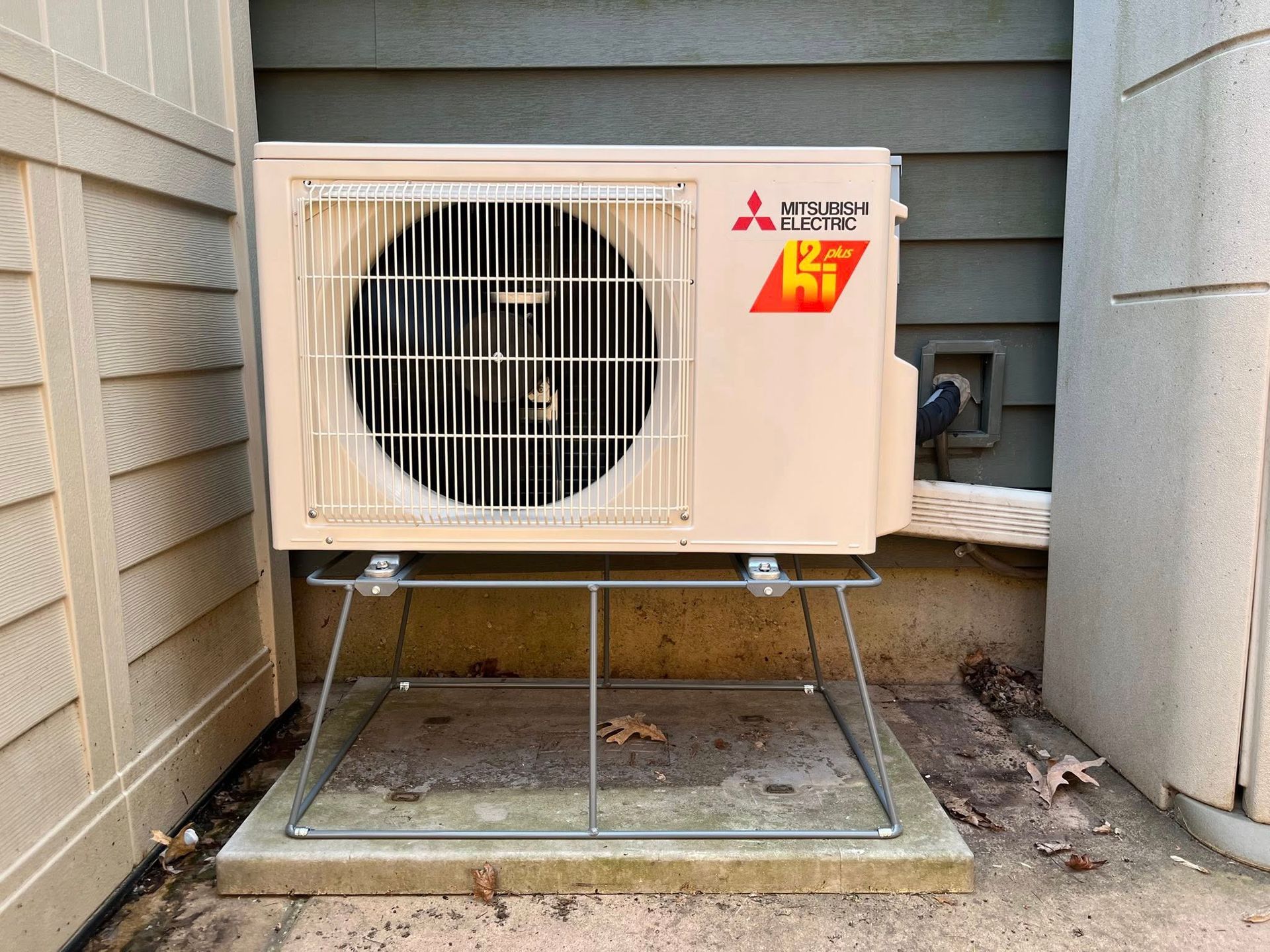 Mitsubishi heat pump unit, beige, mounted outdoors on a concrete pad.
