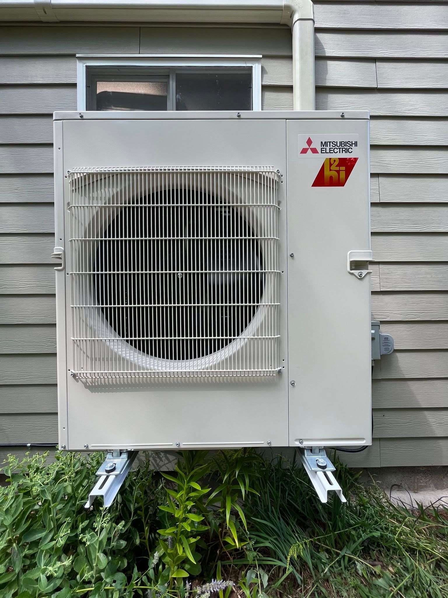 White Mitsubishi air conditioner mounted on a wooden wall above greenery.