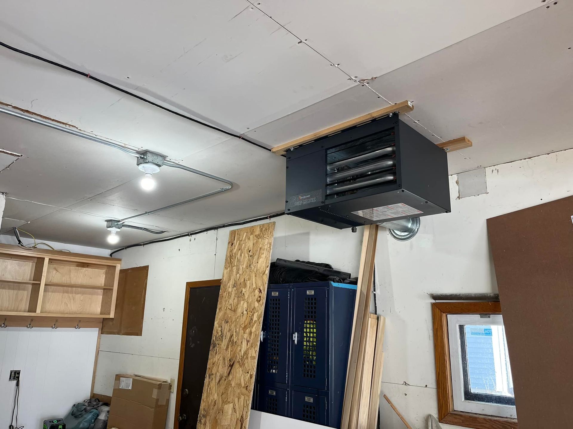 Ceiling-mounted garage heater. Black, rectangular, against white ceiling. Wooden support beams.