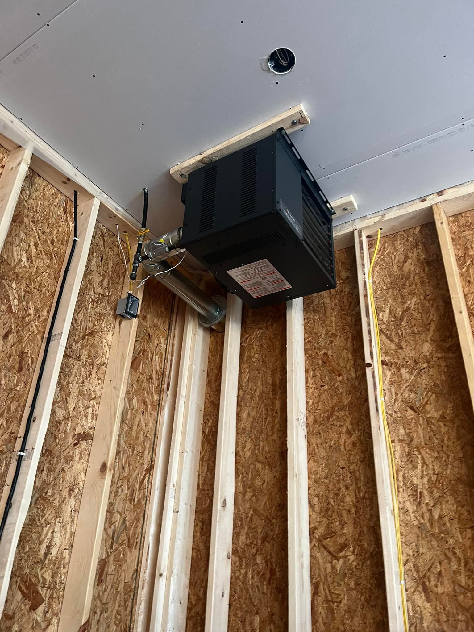 Black ceiling-mounted heater in unfinished room. Wooden studs, wiring, and white ceiling.