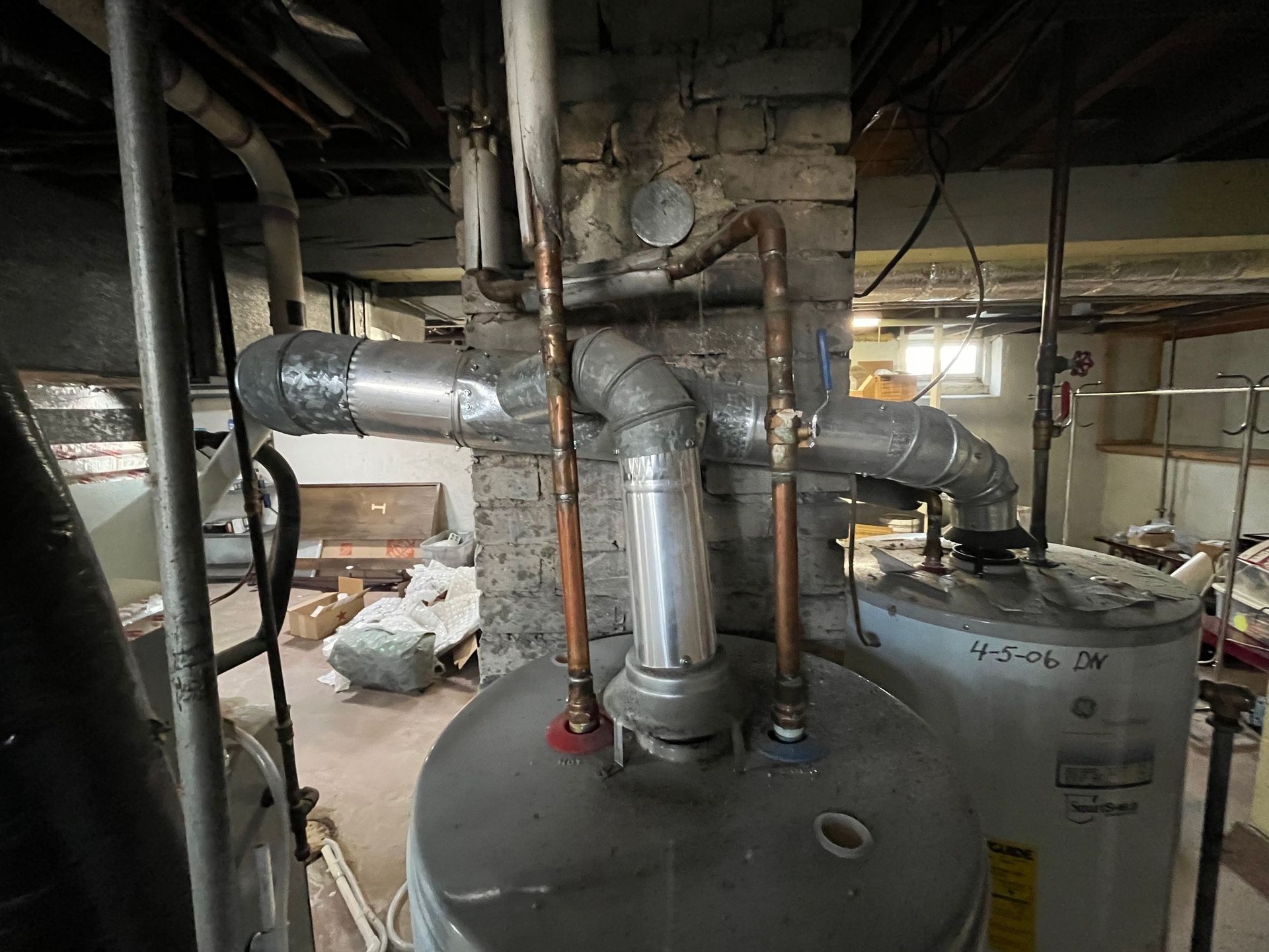Two water heaters and ductwork in a basement setting. Copper pipes and silver ducting are visible.
