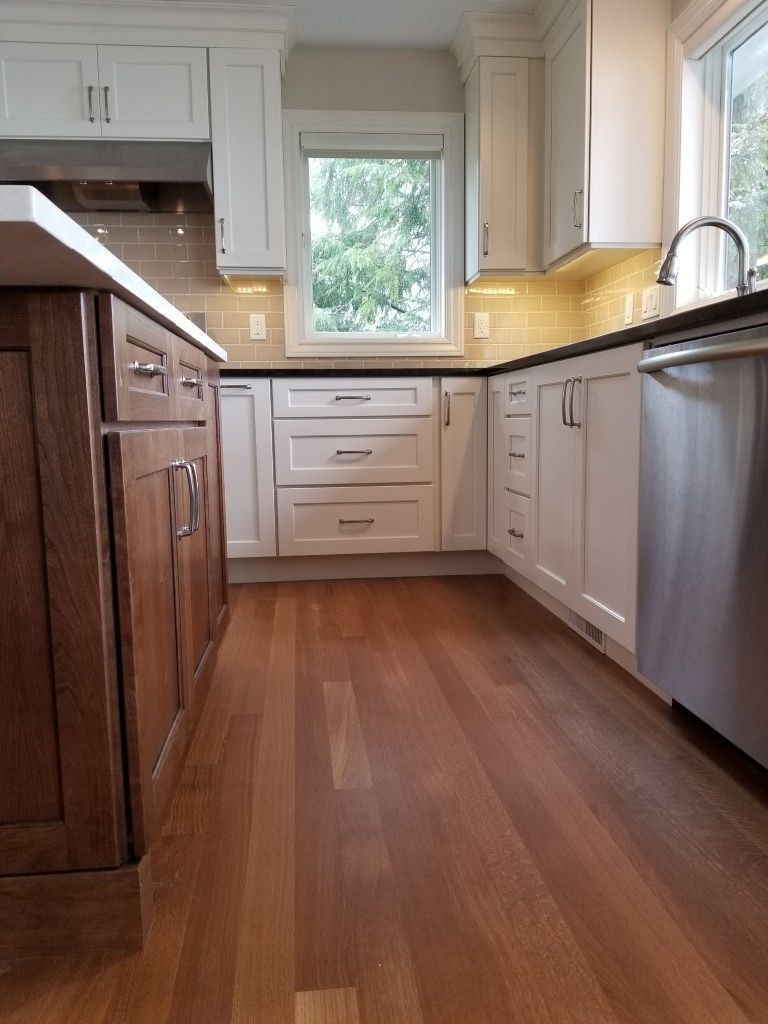 Bright modern kitchen with wood floor, white cabinets, and stainless-steel dishwasher