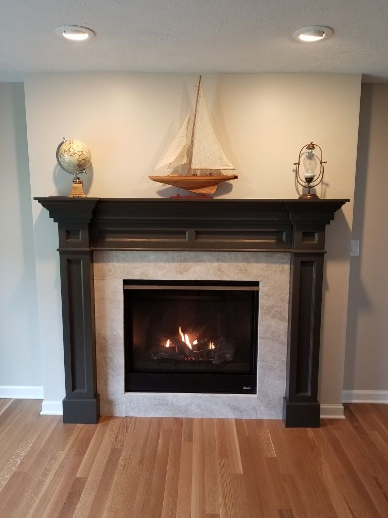 Living room fireplace with dark mantel, lit fire, sailboat decor, and warm wood floors