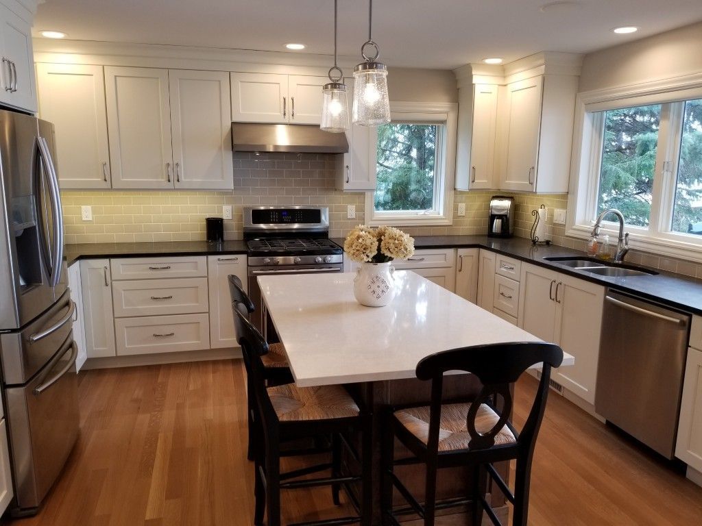 Bright kitchen with white cabinets, central island, stainless appliances, and large windows.