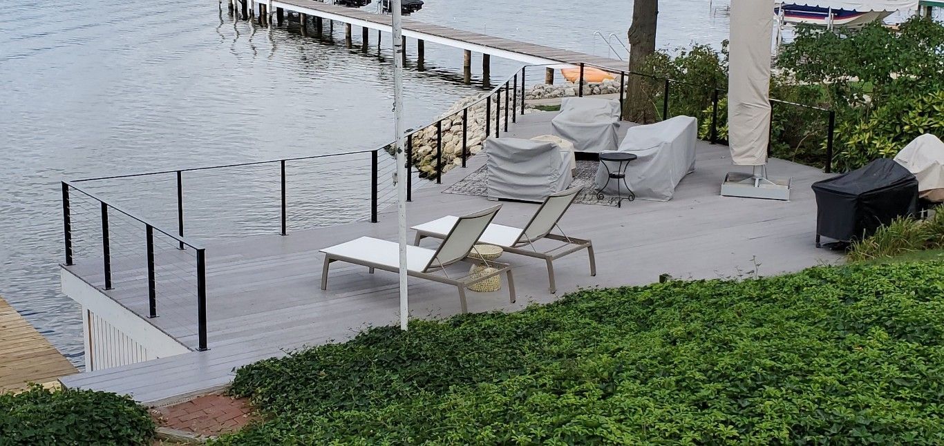 Poolside patio with lounge chairs, white umbrellas, and a black fence beside the water