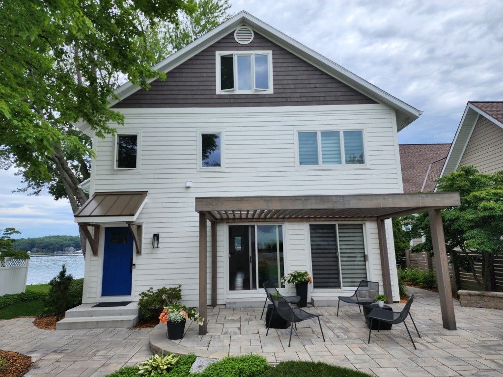 Two-story white house with blue door, porch seating, and lake view under a cloudy sky