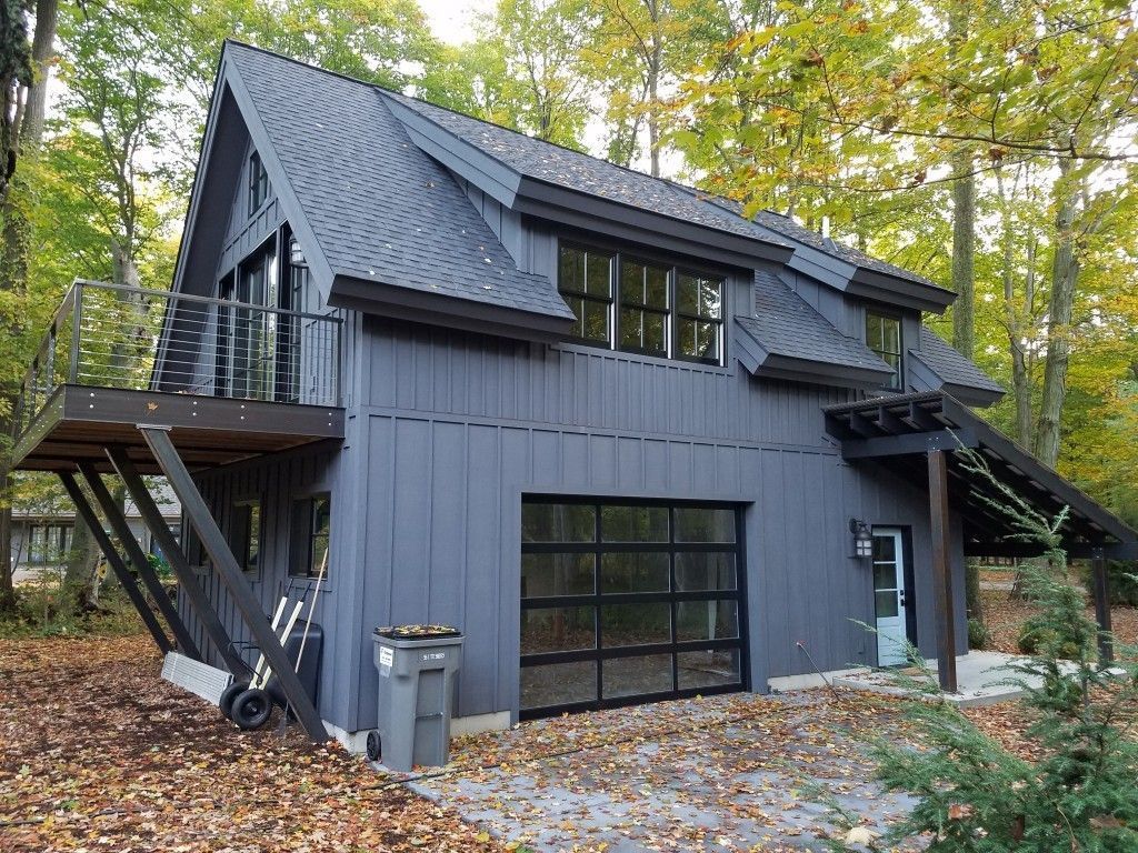 Dark modern cabin with steep roof and black siding in a leafy forest clearing