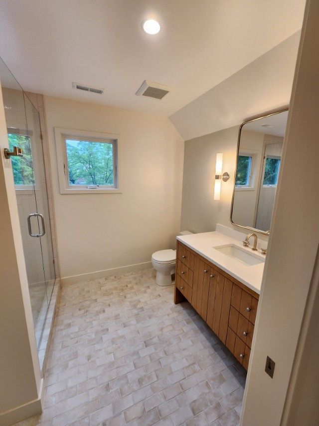 Bright bathroom with walk-in shower, vanity, toilet, and window on the far wall.