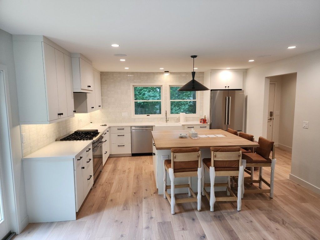 Bright modern kitchen with island, white cabinets, wood flooring, and dining chairs near a window