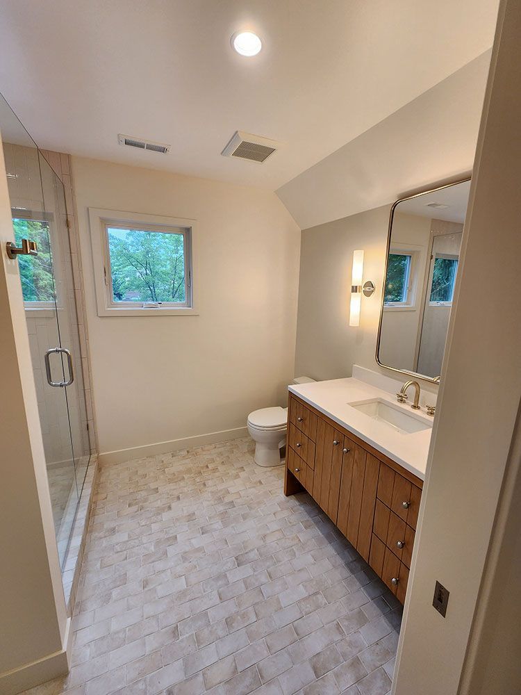 Bathroom with a glass shower, wooden vanity, and neutral-toned tile flooring.