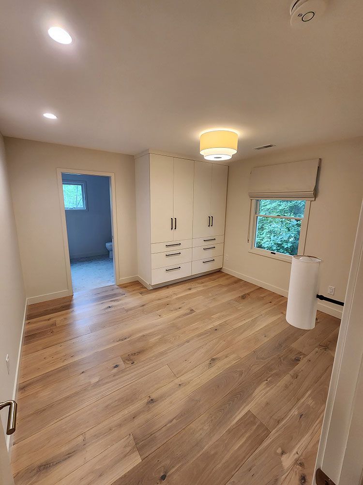Bright bedroom with wood flooring, built-in white cabinets, and a view of a bathroom.