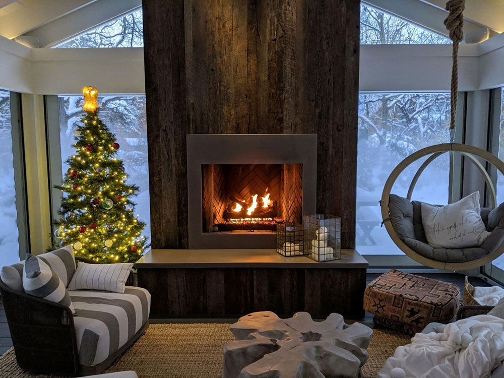 Cozy living room with a fireplace, Christmas tree, and a hanging chair, surrounded by snowy windows.