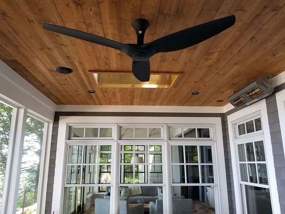 Black ceiling fan, skylight, and heater on wood-paneled ceiling above windows in a sunroom.