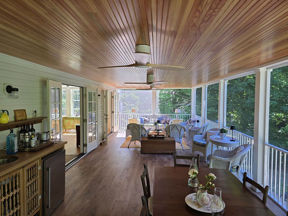 Spacious screened porch with wood ceiling, fan, furniture, and dining area, with doors to the outdoors.