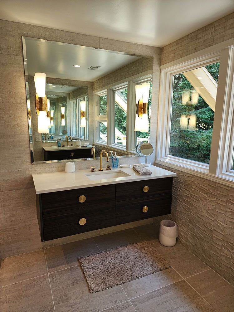 Modern bathroom with floating dark wood vanity, gold fixtures, and large mirror.