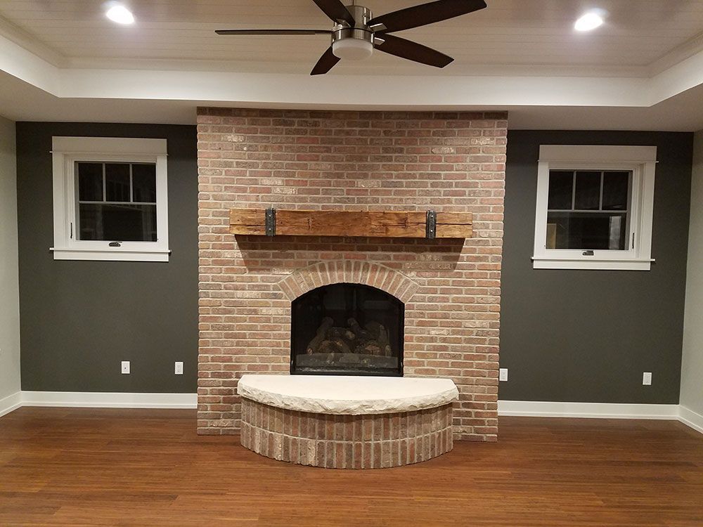 Fireplace with brick surround and wooden mantel in a room with dark gray walls and wood floor.
