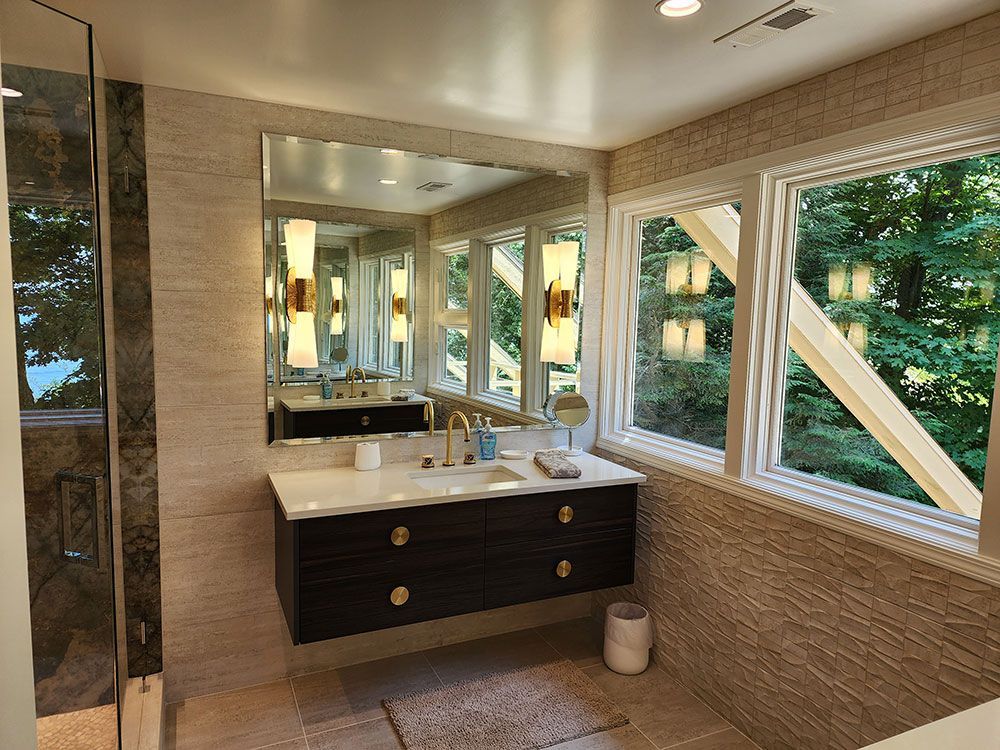 Bathroom with floating vanity, large mirror, gold fixtures, and window overlooking greenery.