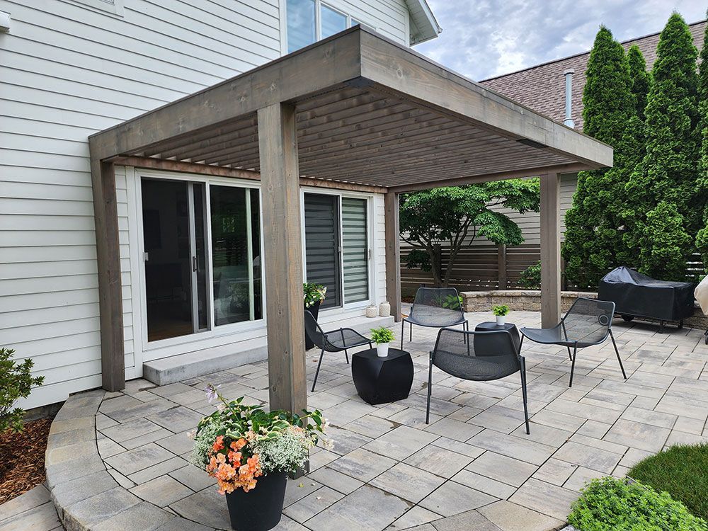 Patio with gray pergola, seating, and potted flowers near a sliding glass door.