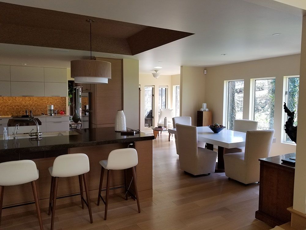 A modern, open-concept kitchen and dining area. Light wood floors and white furniture contrast with the dark countertops.