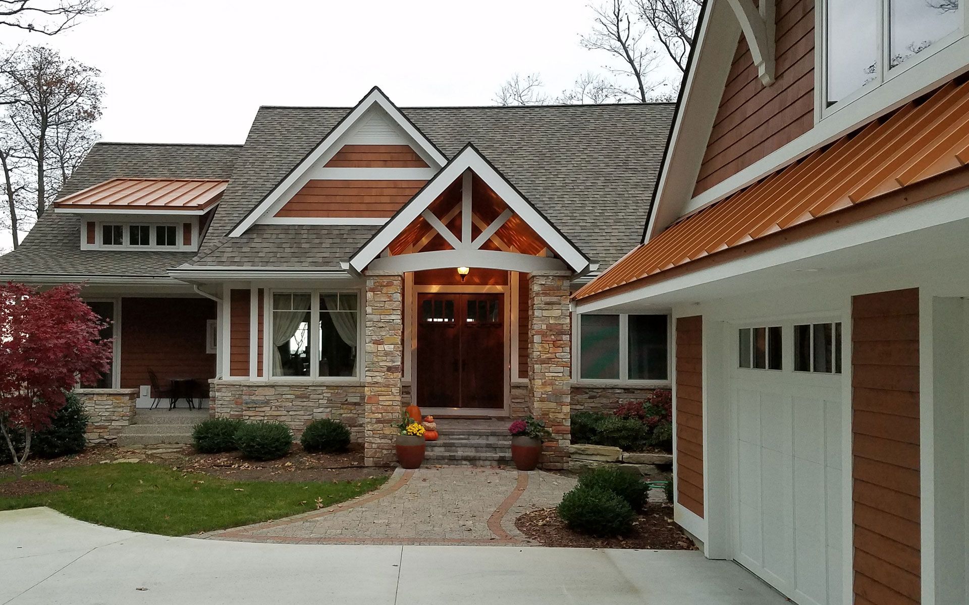 House exterior with stone and wood siding, copper roofing, and a white garage door.