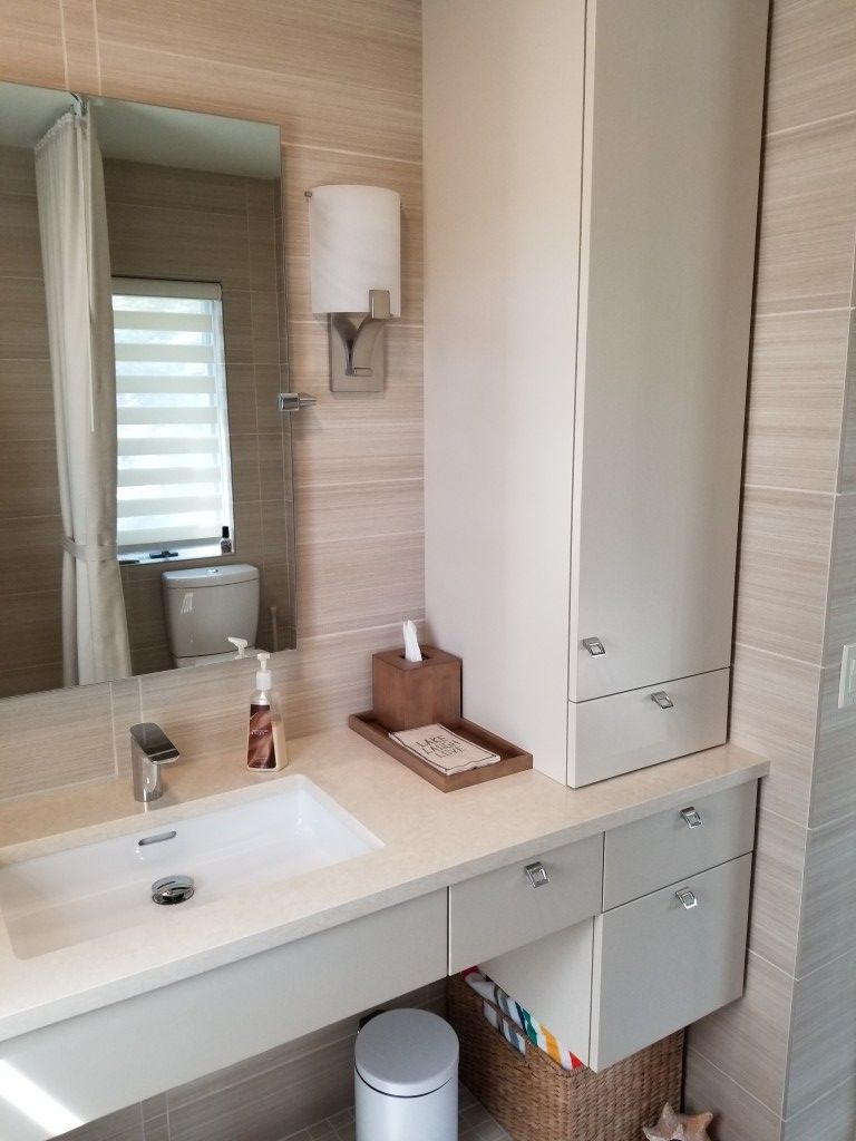 Modern bathroom vanity with sink, mirror, wall sconce, and light wood cabinetry.