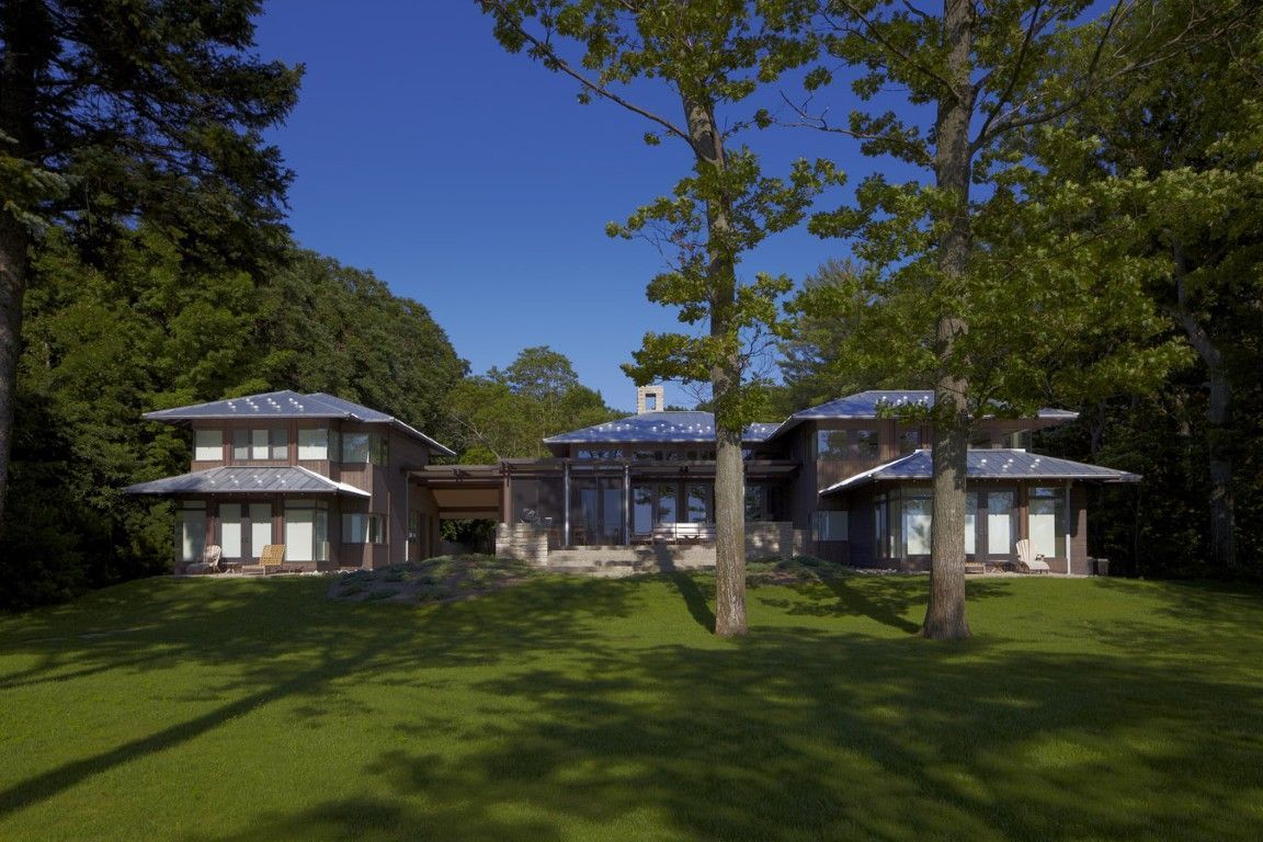 Large house with white columns and a glass center pavilion on a green lawn under trees.
