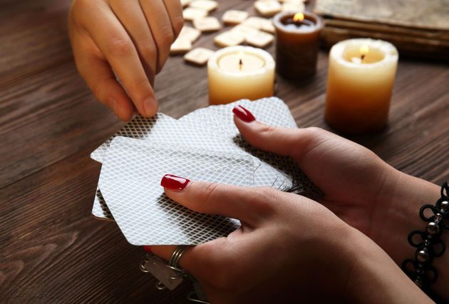 Hands shuffling tarot cards on a wooden table, candles and runes in the background.