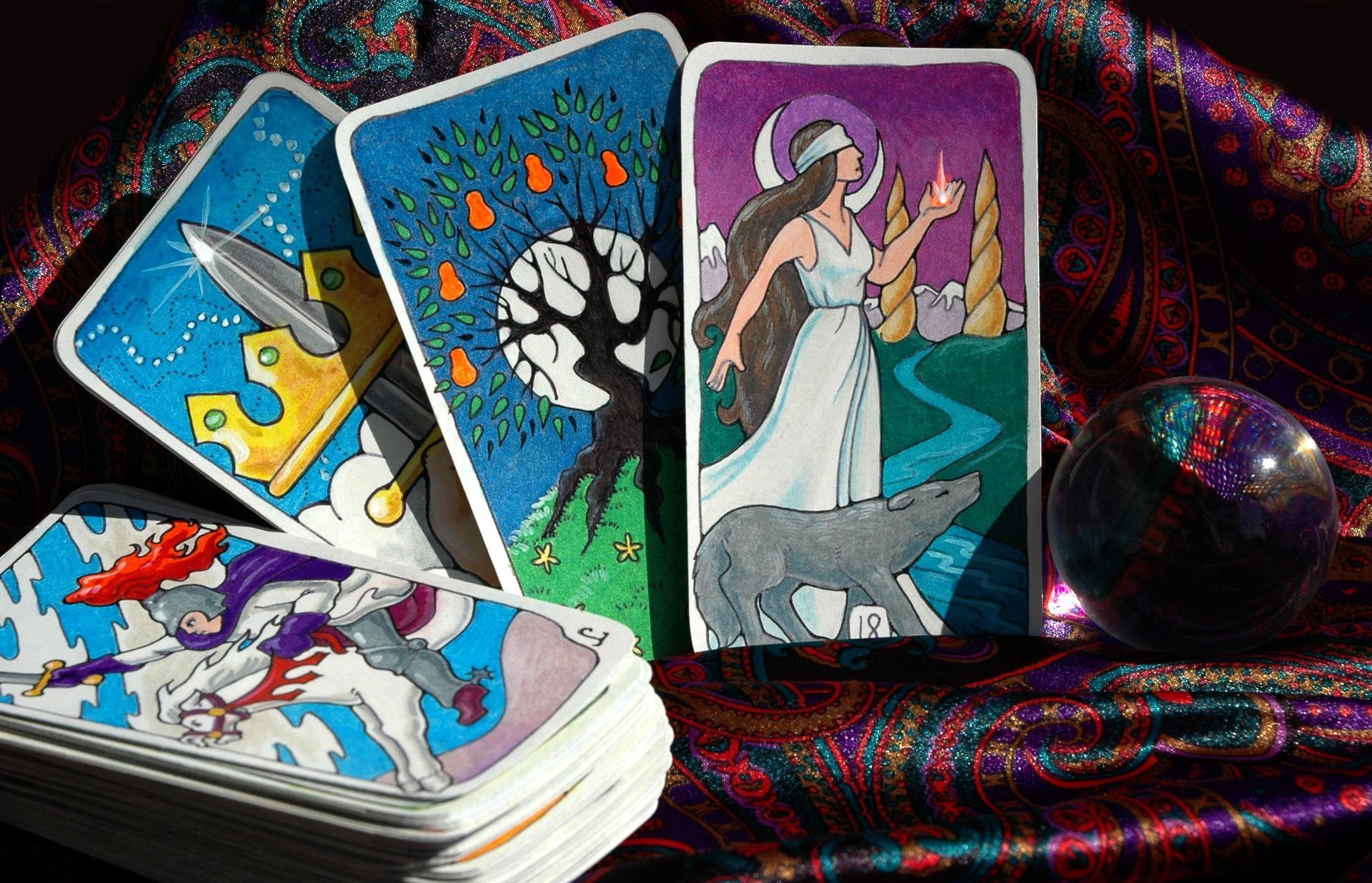Tarot cards displayed on a patterned cloth, with a crystal ball. Cards show illustrations.