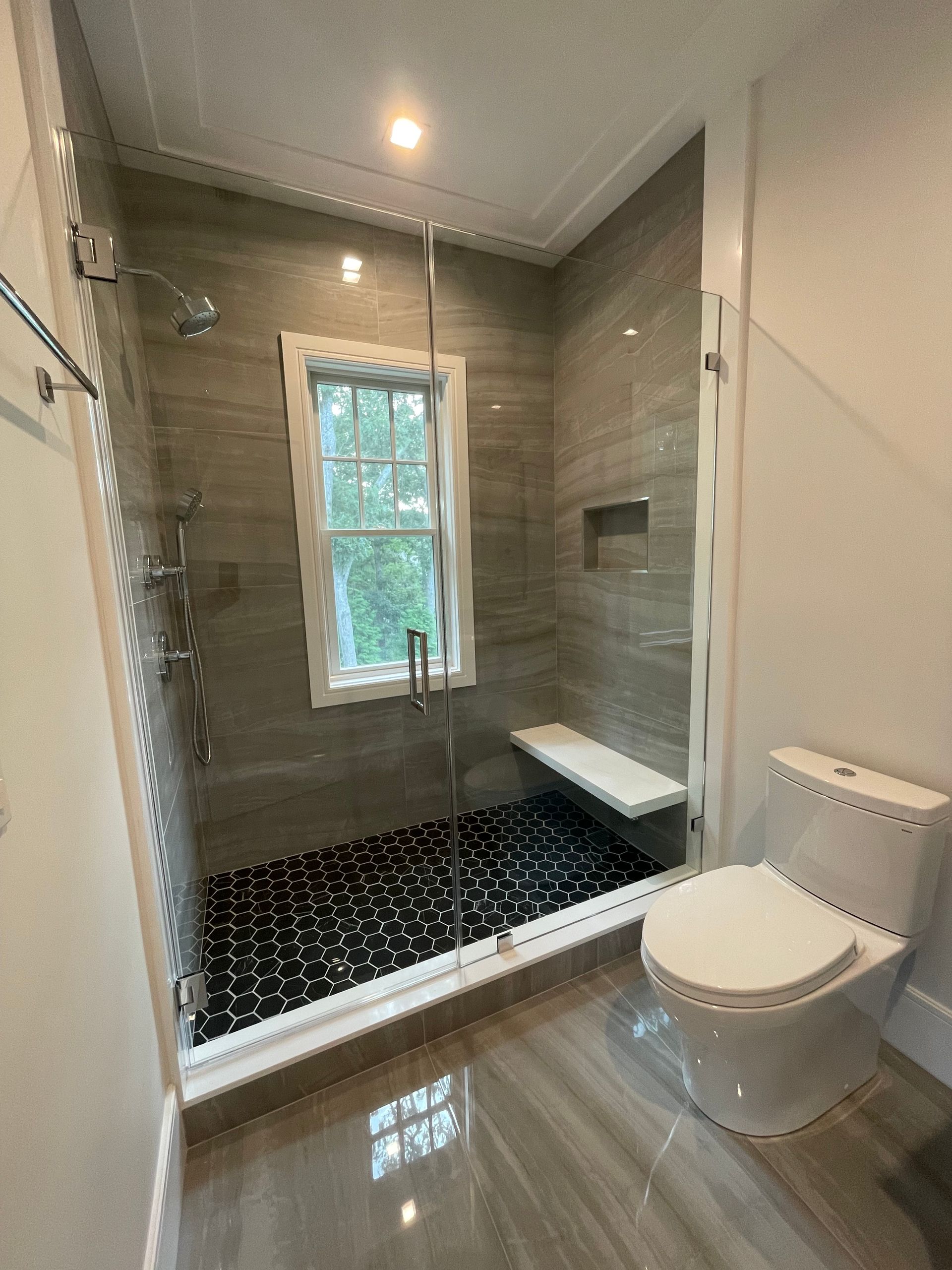 A bathroom with a toilet , shower and window.