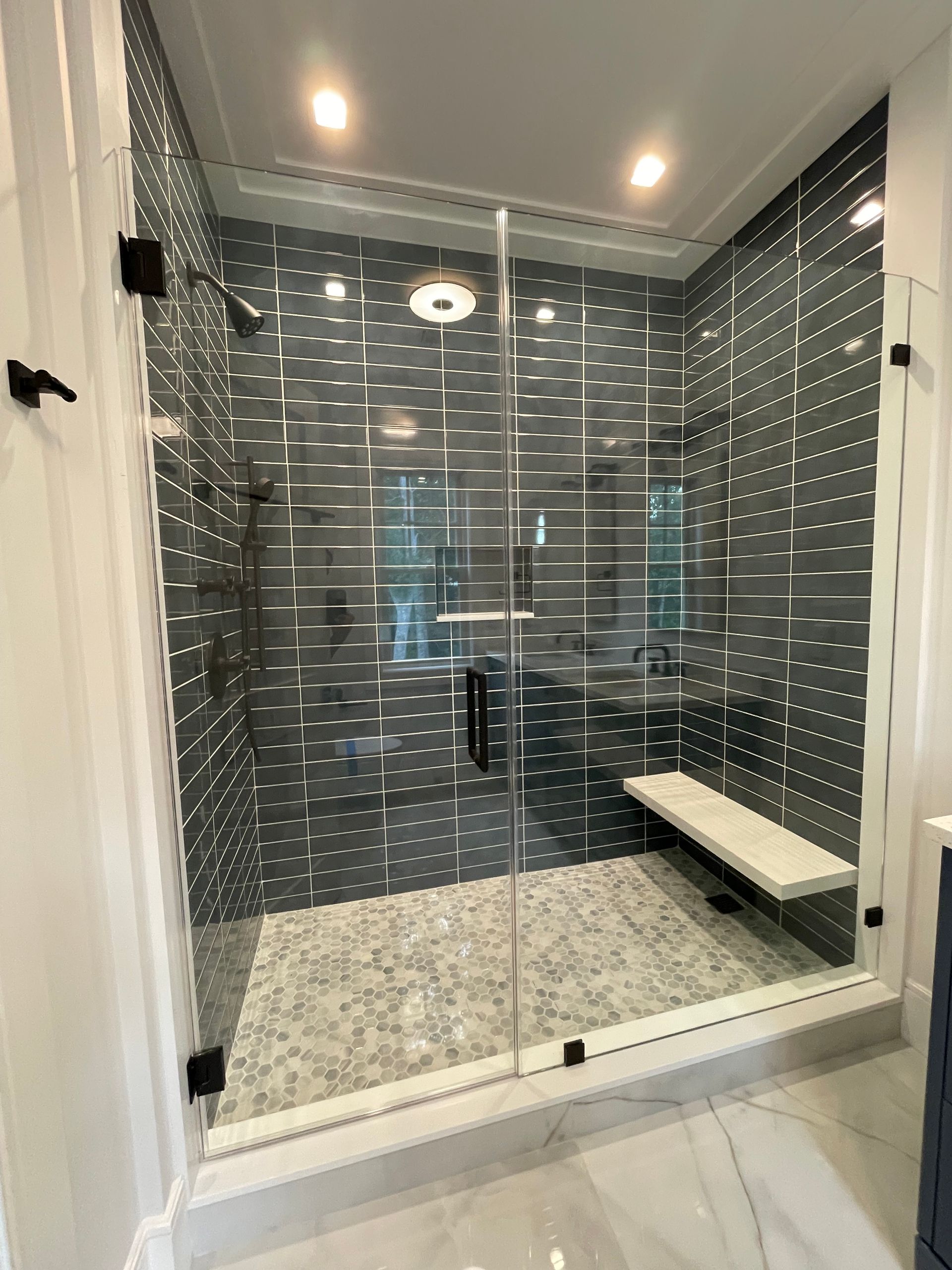 A bathroom with a walk in shower with a glass door and a bench.