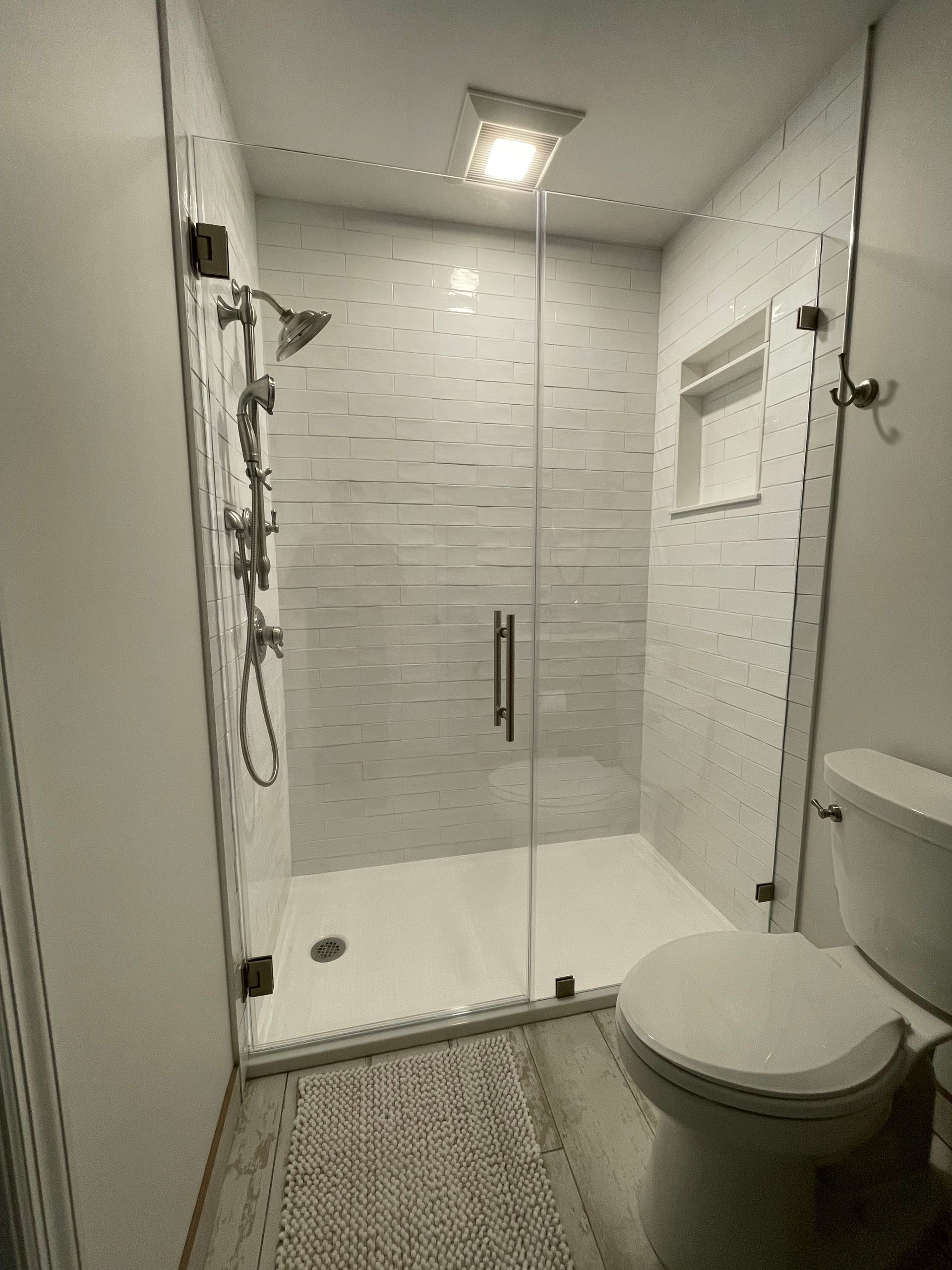 A bathroom with a toilet , shower , and glass door.